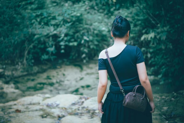 Woman in black dress walks toward forest stream