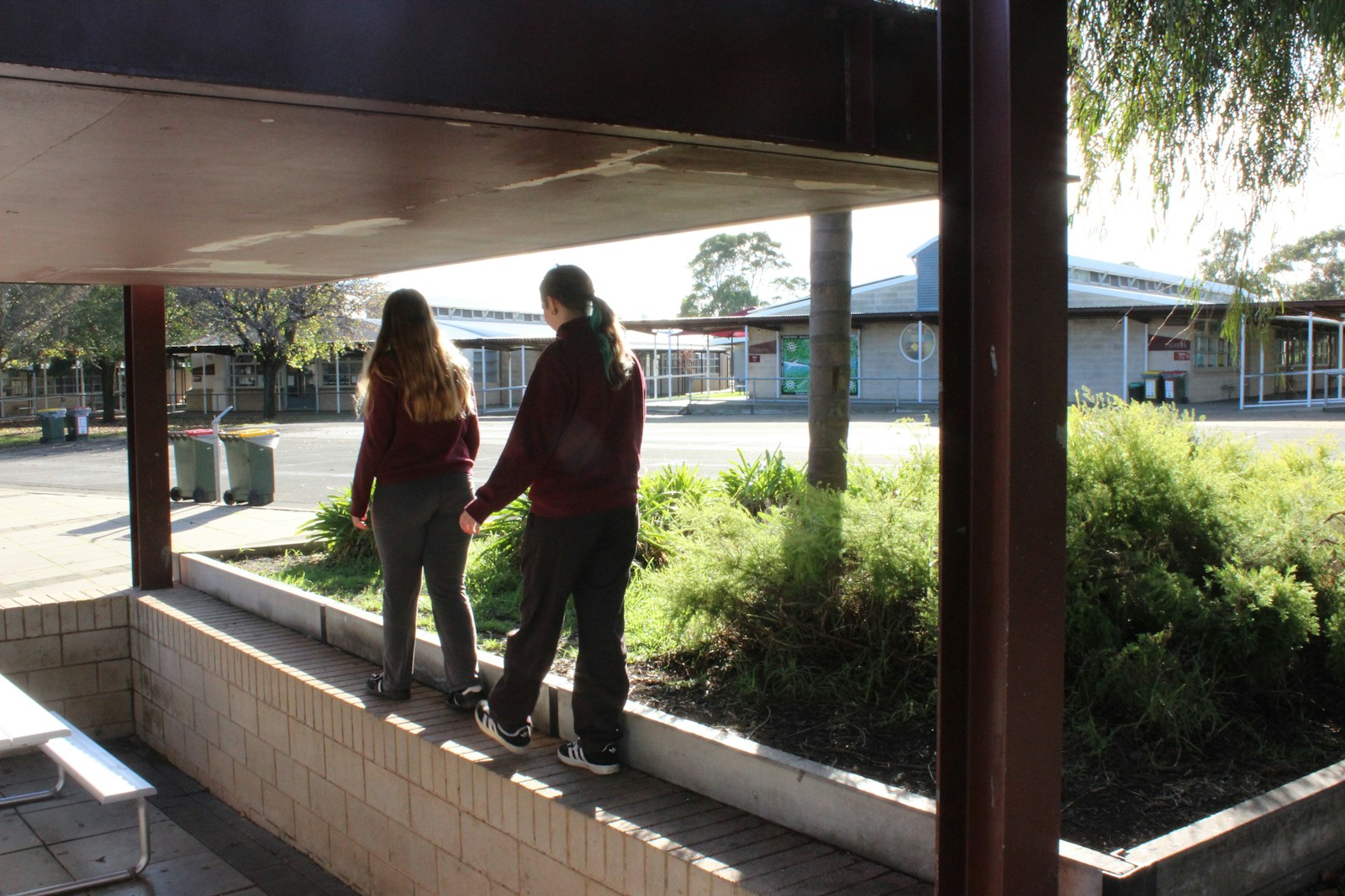 Two students walk on a low wall outdoors.
