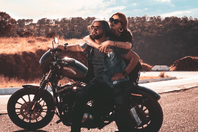 A couple embraces while sitting on a Harley Davidson motorbike on a scenic road.