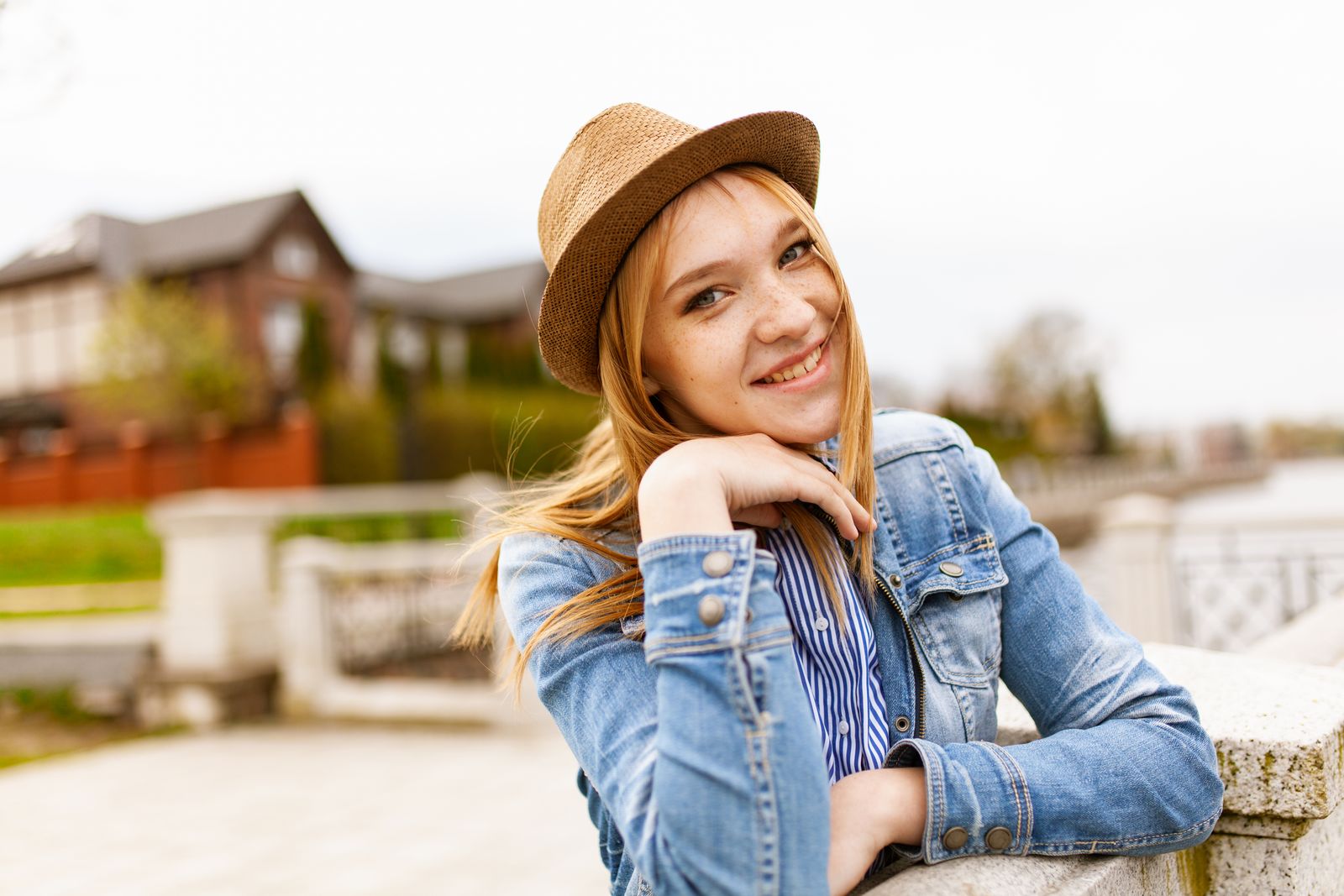 Smiling woman in denim and a hat enjoying a sunny outdoor day with a scenic background.