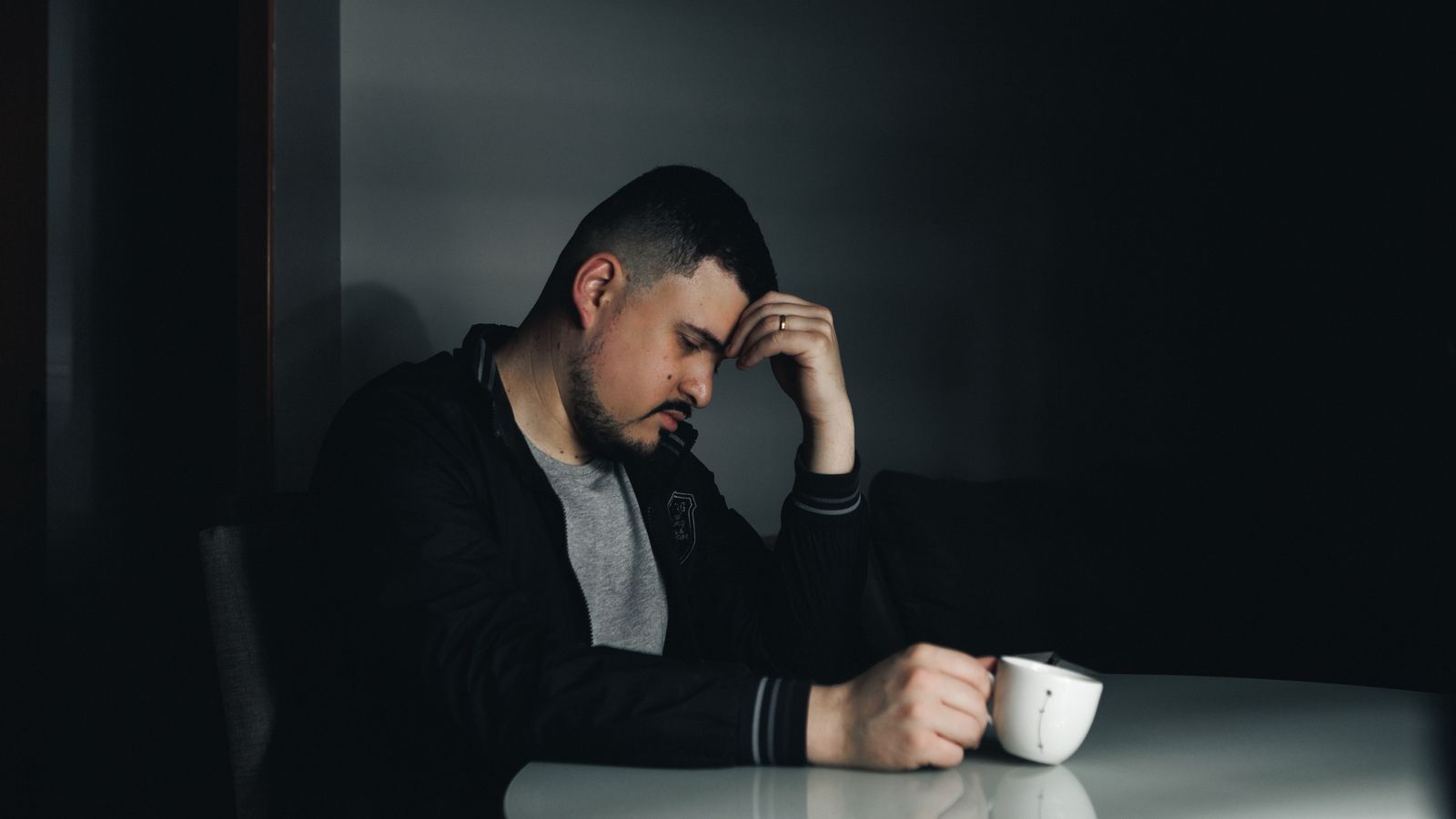 A thoughtful man in a dark room holding a coffee cup, depicting a moody morning scene.