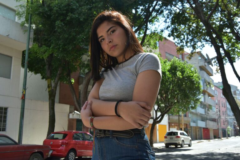 Brunette woman confidently poses in an urban neighborhood street.
