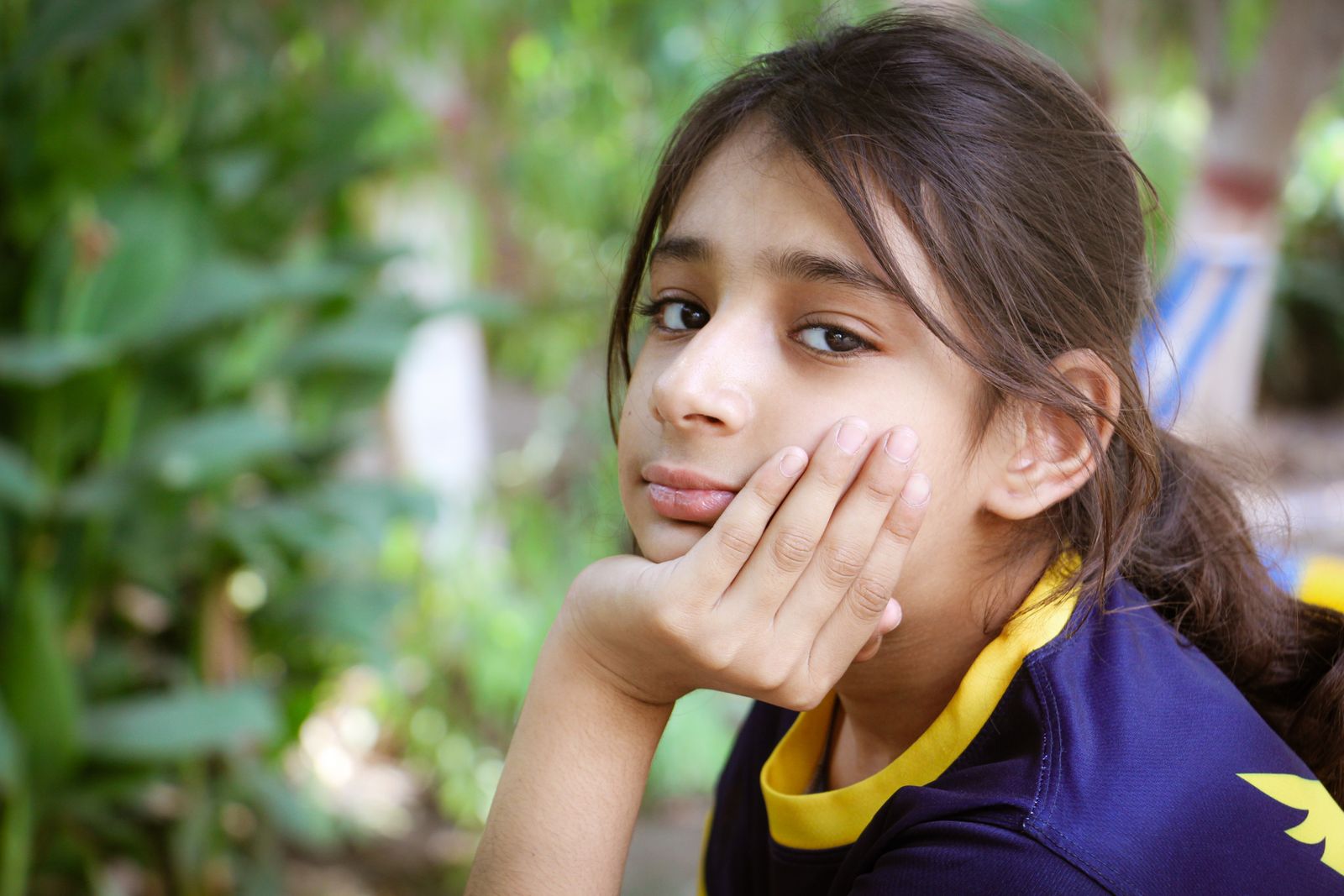 A young girl relaxing in a park, with a thoughtful expression among lush greenery.