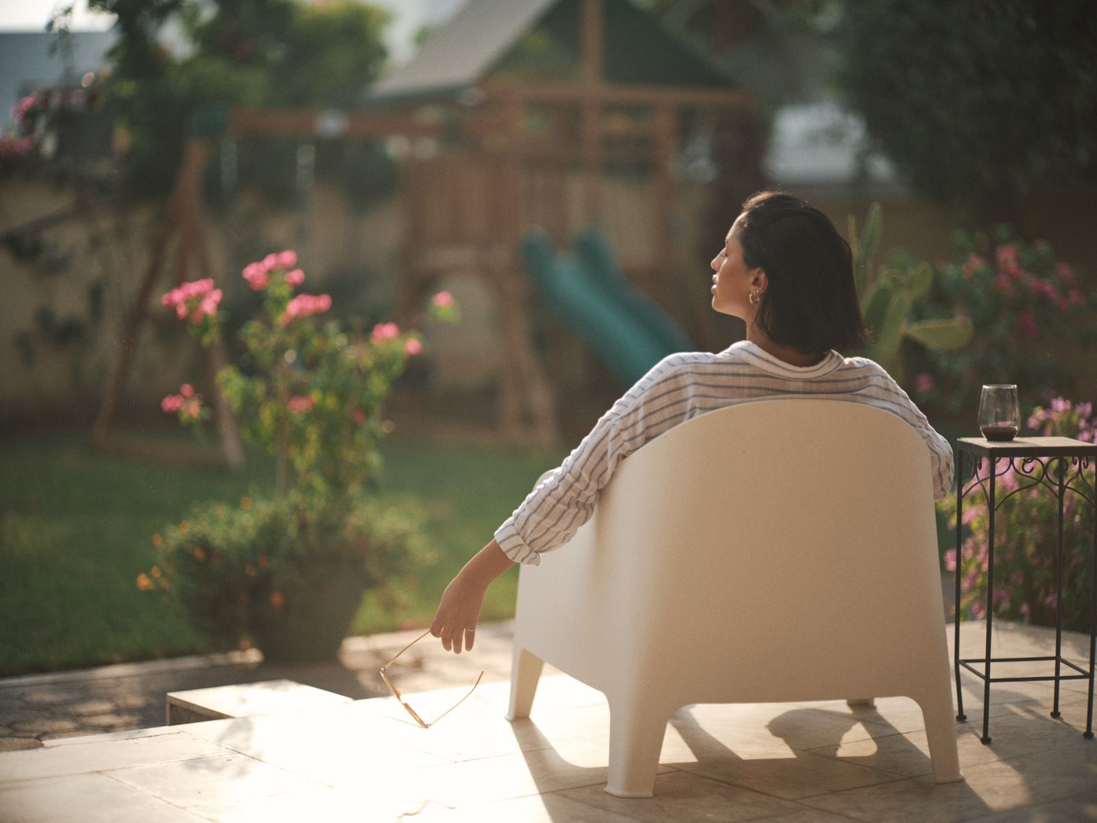 Woman enjoying a quiet moment in a sunlit garden chair, surrounded by nature.