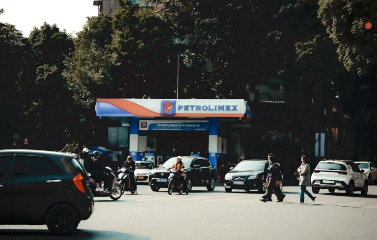 Busy street scene with vehicles and pedestrians at a Petrolimex gas station under daylight.