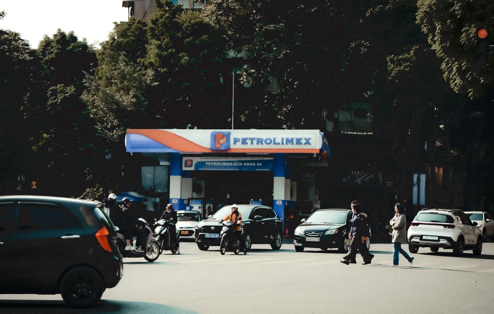 Busy street scene with vehicles and pedestrians at a Petrolimex gas station under daylight.