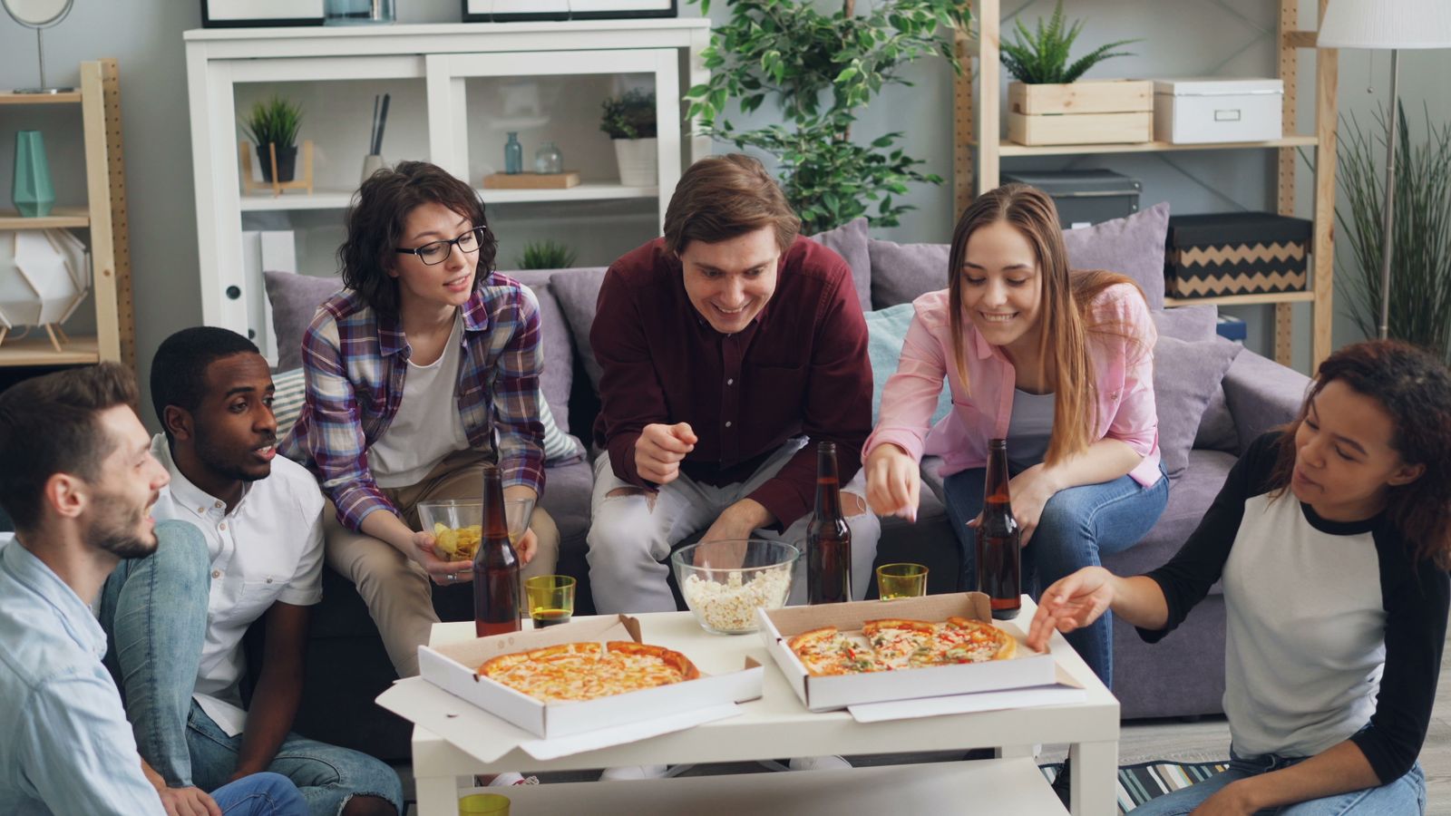 A diverse group of young friends enjoying pizza and drinks together indoors.