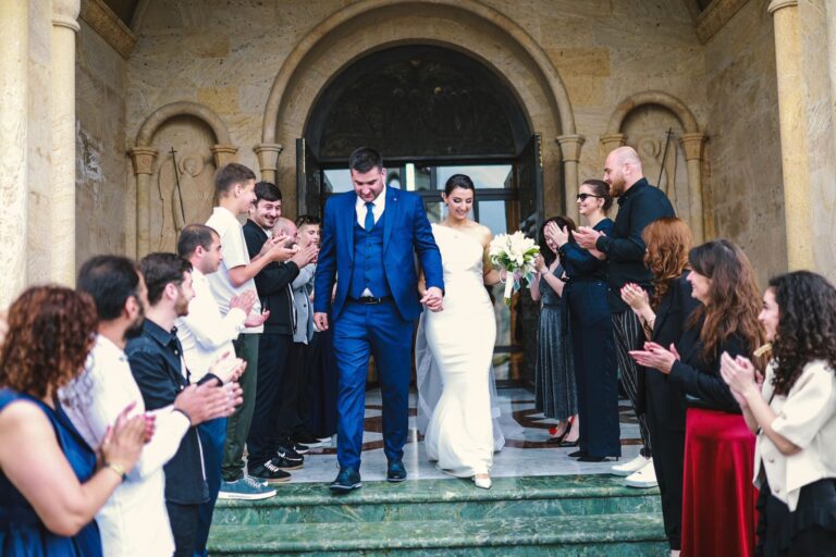 Bride and groom exiting a church, surrounded by applauding guests in an outdoor wedding ceremony.