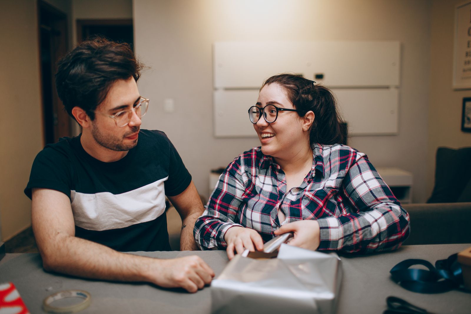 Man and woman happily wrapping a gift inside a cozy room, fostering togetherness.