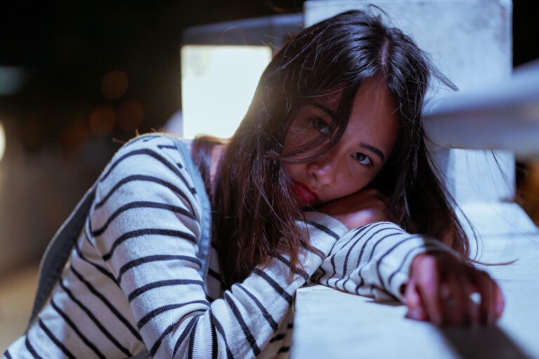 A woman in a striped sweater poses contemplatively at night in a soft focus setting.