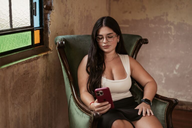 A young woman seated on a chair indoors, using her smartphone, showcasing relaxation and technology.