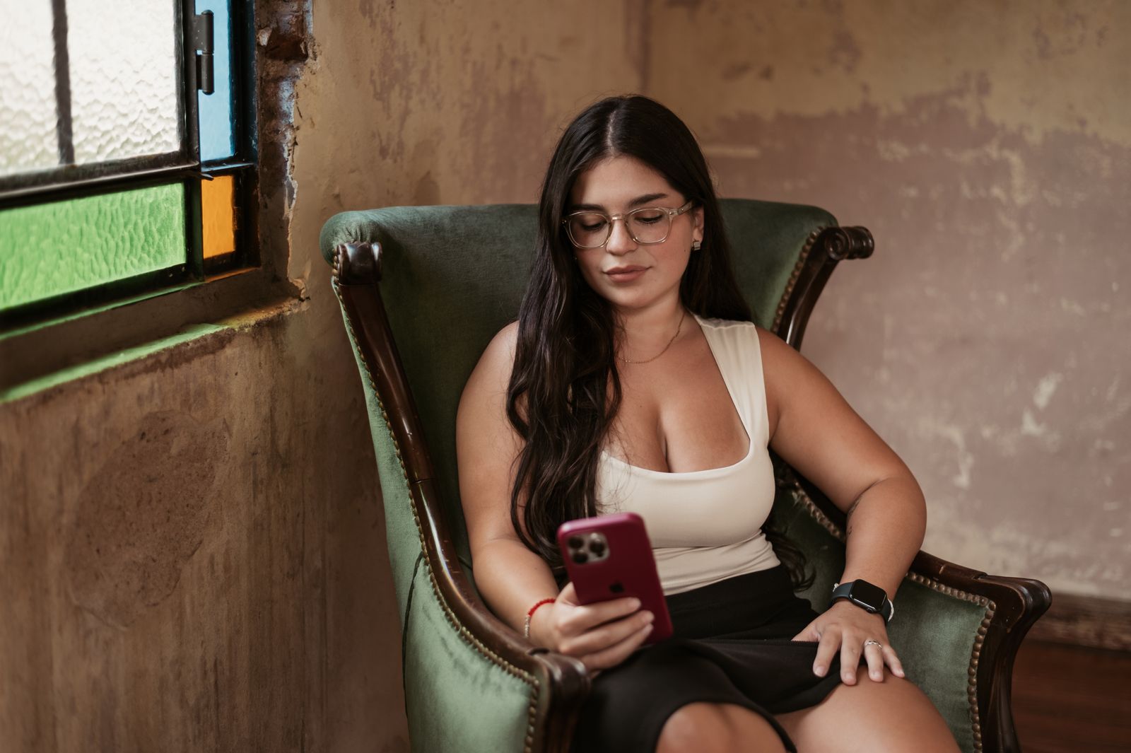 A young woman seated on a chair indoors, using her smartphone, showcasing relaxation and technology.