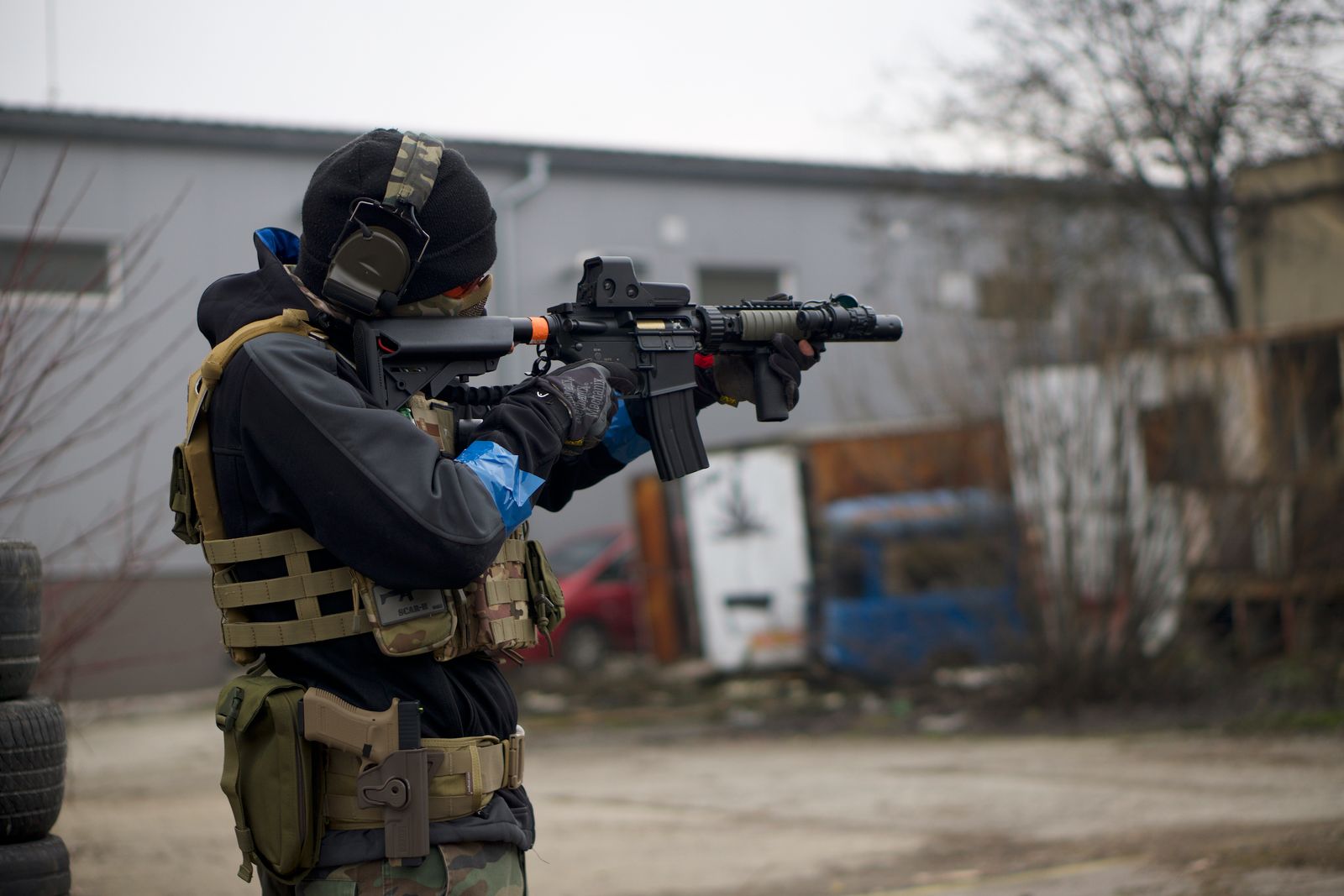 An airsoft player in full tactical gear aiming a rifle outdoors, showing action and focus.