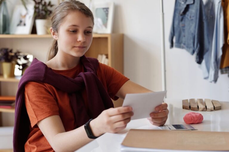 A teenage girl thoughtfully examines photos at her desk, lost in memories.