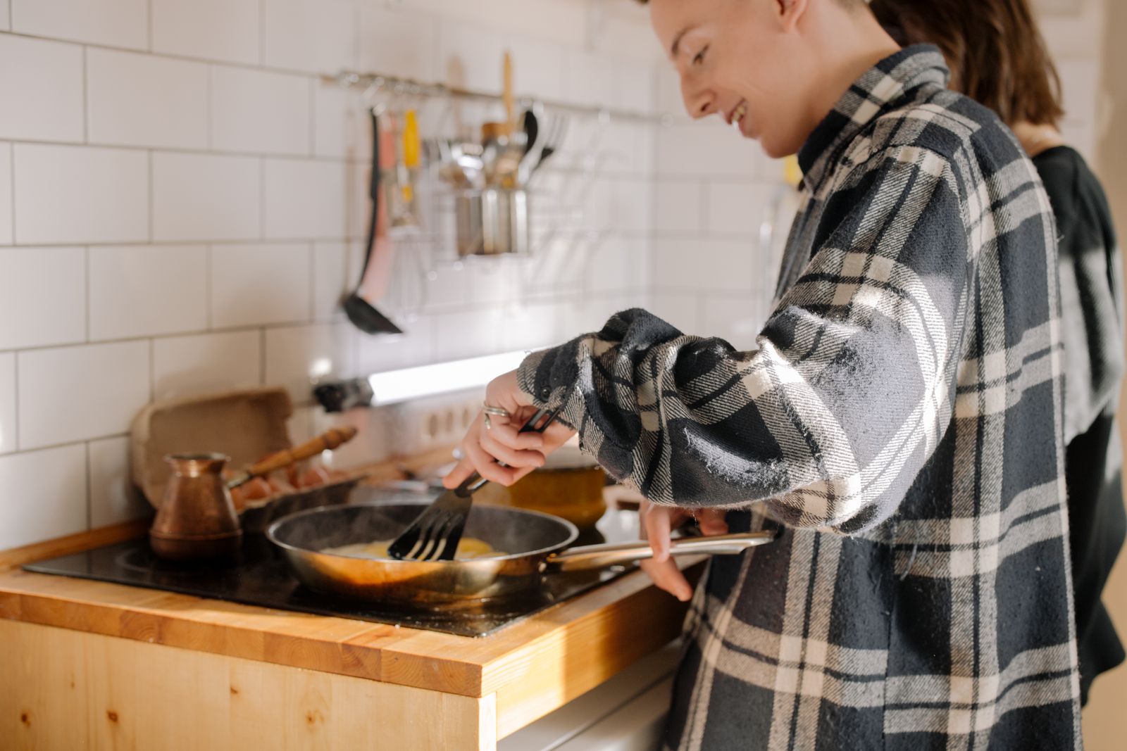 A young man in a checkered shirt cooking breakfast on the stove in a modern kitchen interior.