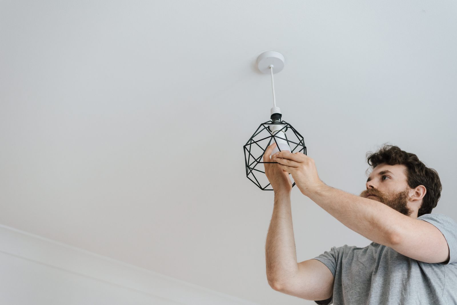 From below of male screwing light bulb into new fashionable lamp during renovation work in apartment