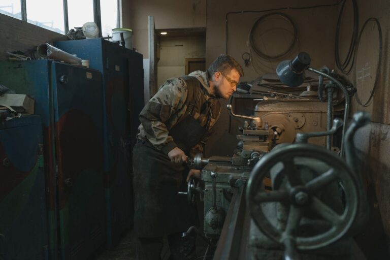 Caucasian man operating a lathe in an industrial workshop setting, focused on precision work.