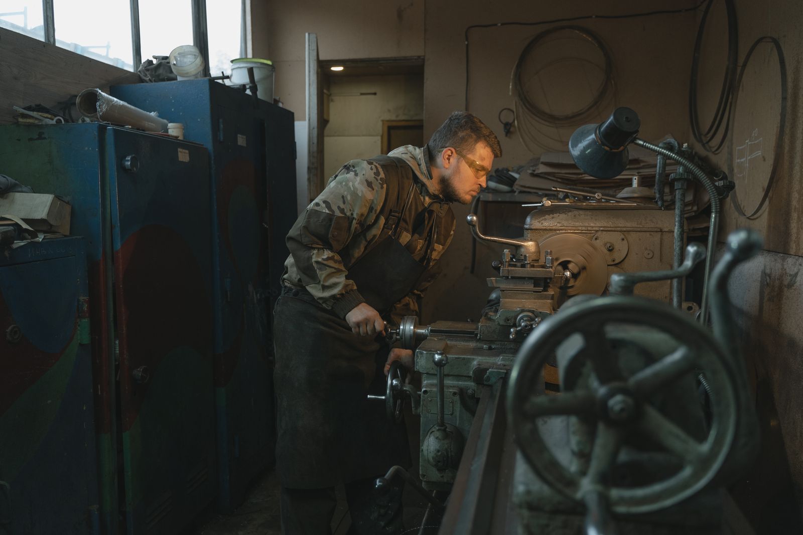 Caucasian man operating a lathe in an industrial workshop setting, focused on precision work.