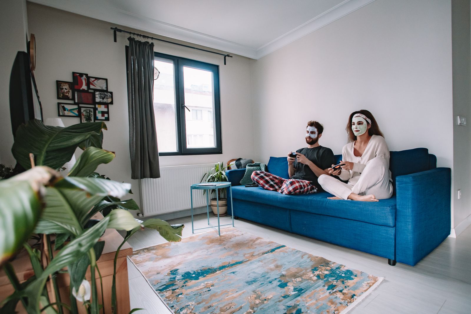 Couple enjoying video games on a sofa while applying relaxing face masks at home.