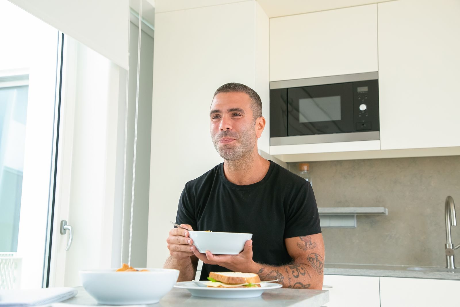 A man with tattoos enjoys breakfast at his modern home kitchen table.
