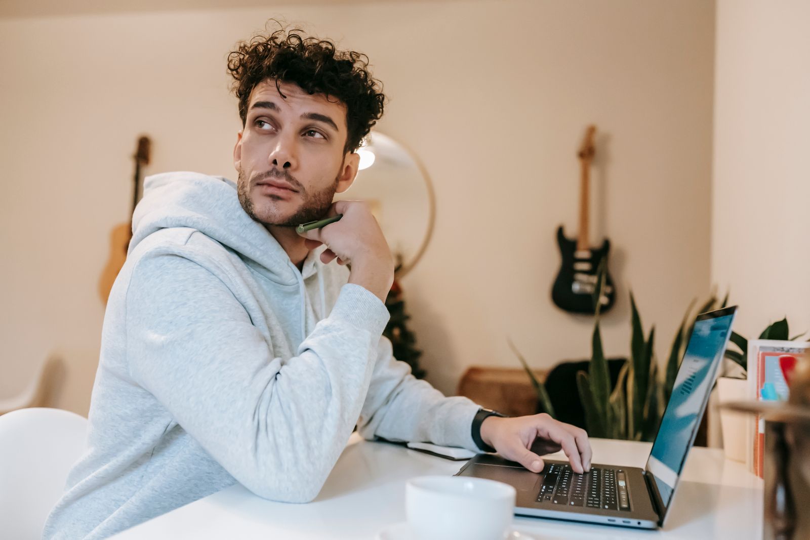Concentrated bearded freelancer with curly hair in casual clothes browsing laptop while working at home and looking away in daytime