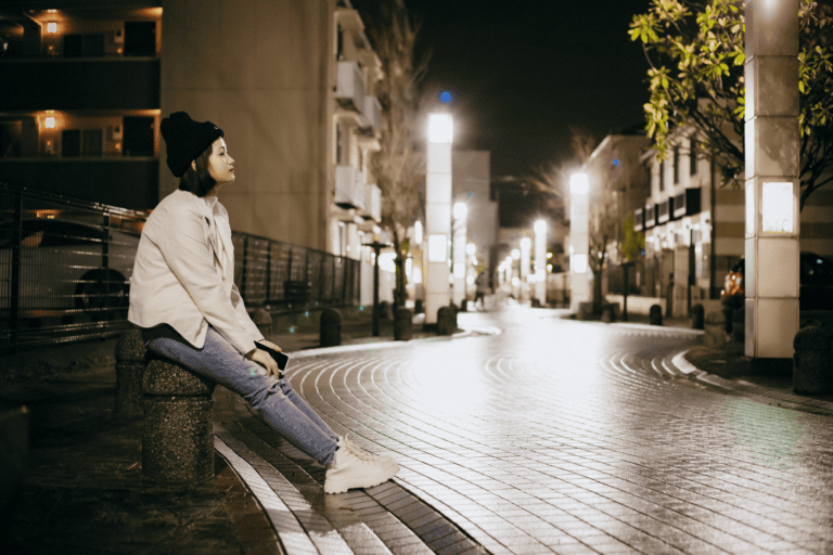 Woman sitting on a bench in an illuminated urban street at night, reflecting a peaceful moment.