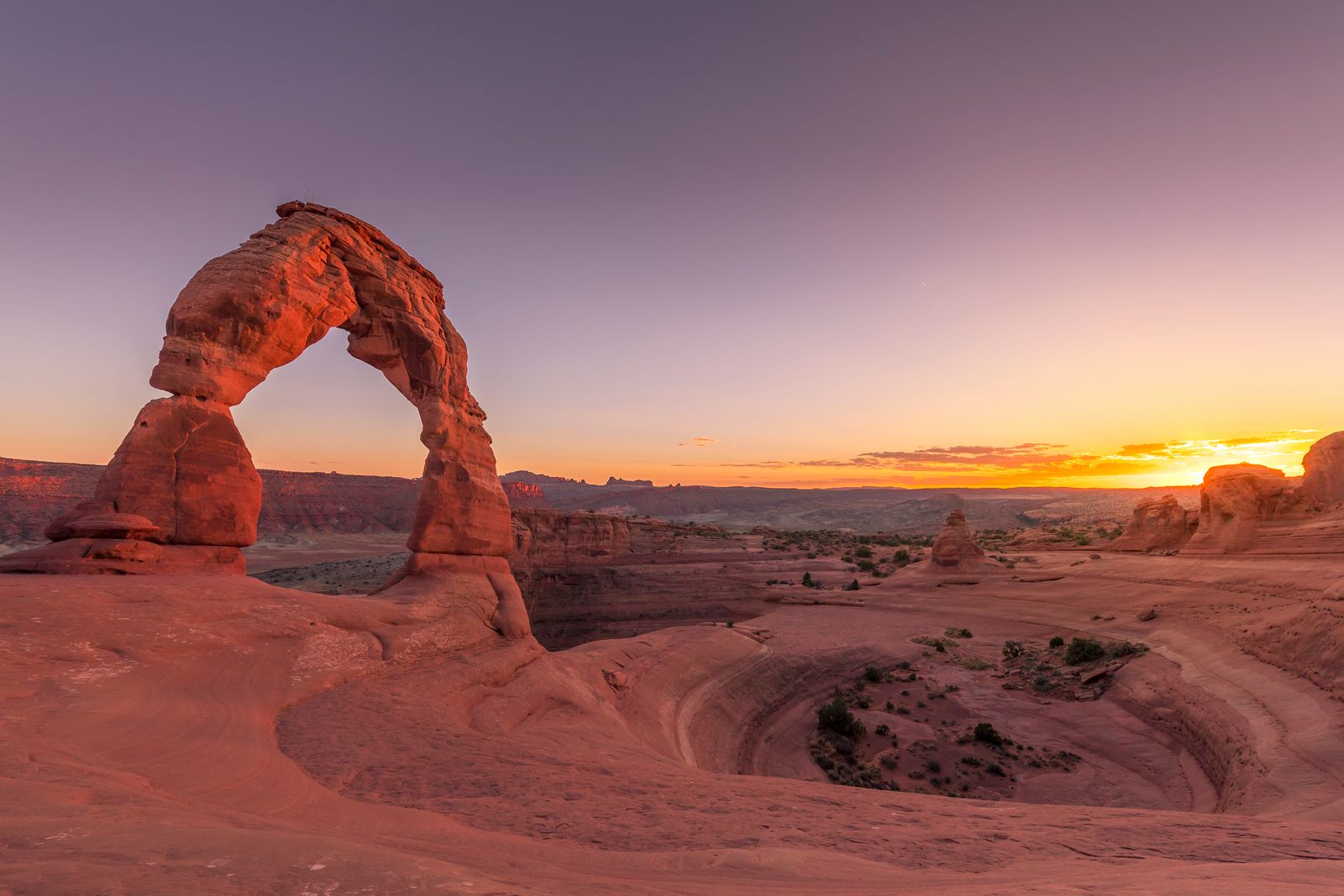 Breathtaking view of Delicate Arch in Arches National Park at sunset, showcasing vibrant skies and rugged landscape.