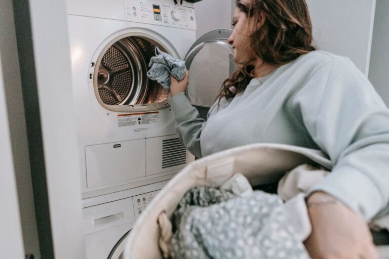 Side view of serious female in casual wear putting laundry into modern washing machine while doing housework in light room at home