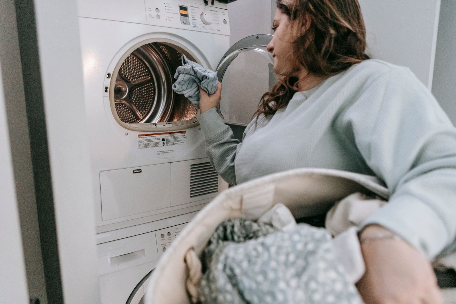 Side view of serious female in casual wear putting laundry into modern washing machine while doing housework in light room at home