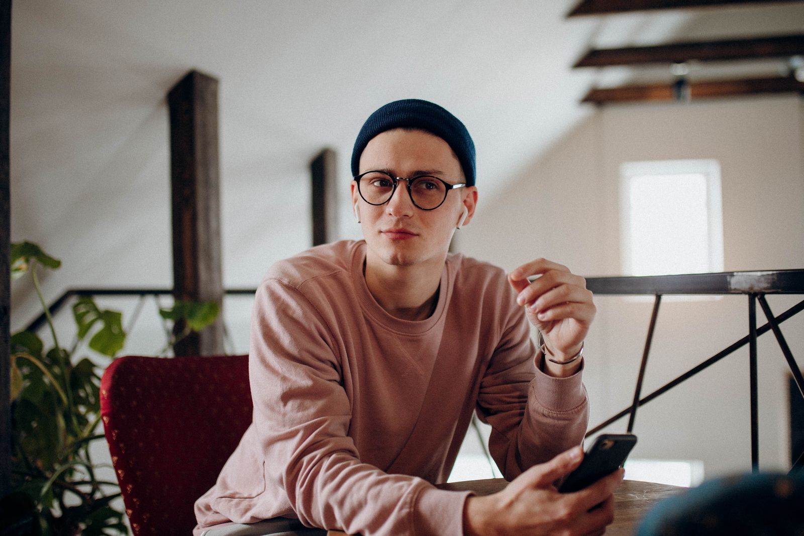 Casual young man in beanie and glasses using smartphone indoors.