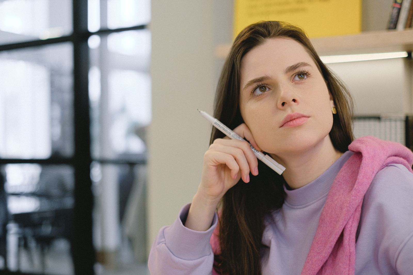 Thoughtful young female millennial with long dark hair in casual outfit touching face and looking away dreamily during lesson in modern classroom