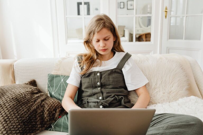 Teenage girl sitting on sofa, concentrating on her laptop in a cozy room, studying.