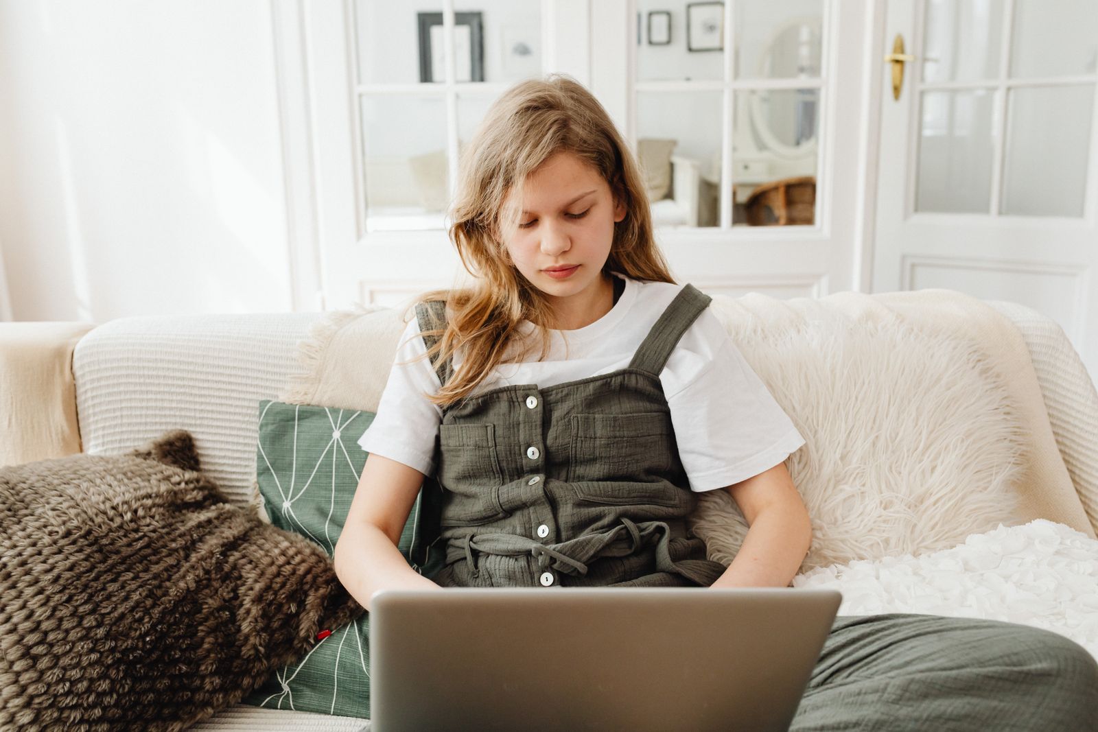 Teenage girl sitting on sofa, concentrating on her laptop in a cozy room, studying.