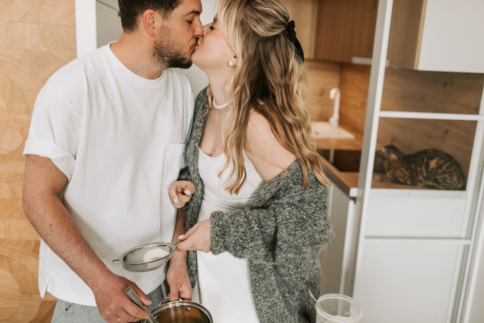 A loving couple shares a kiss while preparing a meal in a cozy kitchen setting.