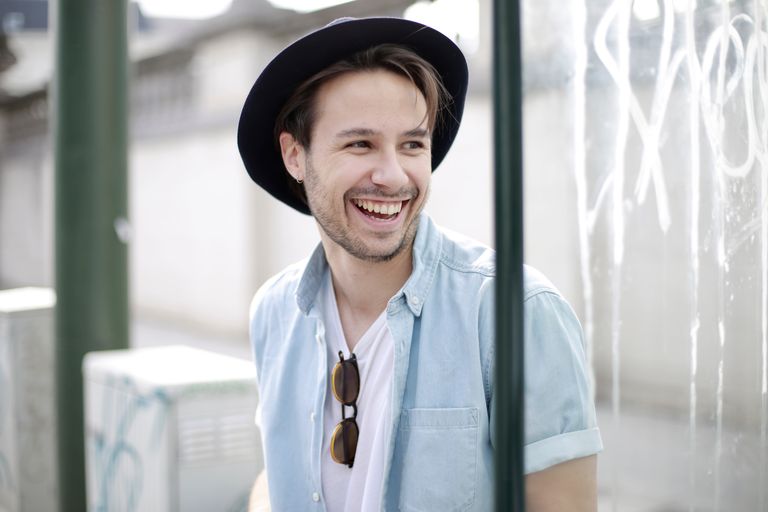 A cheerful young man in a hat and sunglasses smiling brightly outdoors.