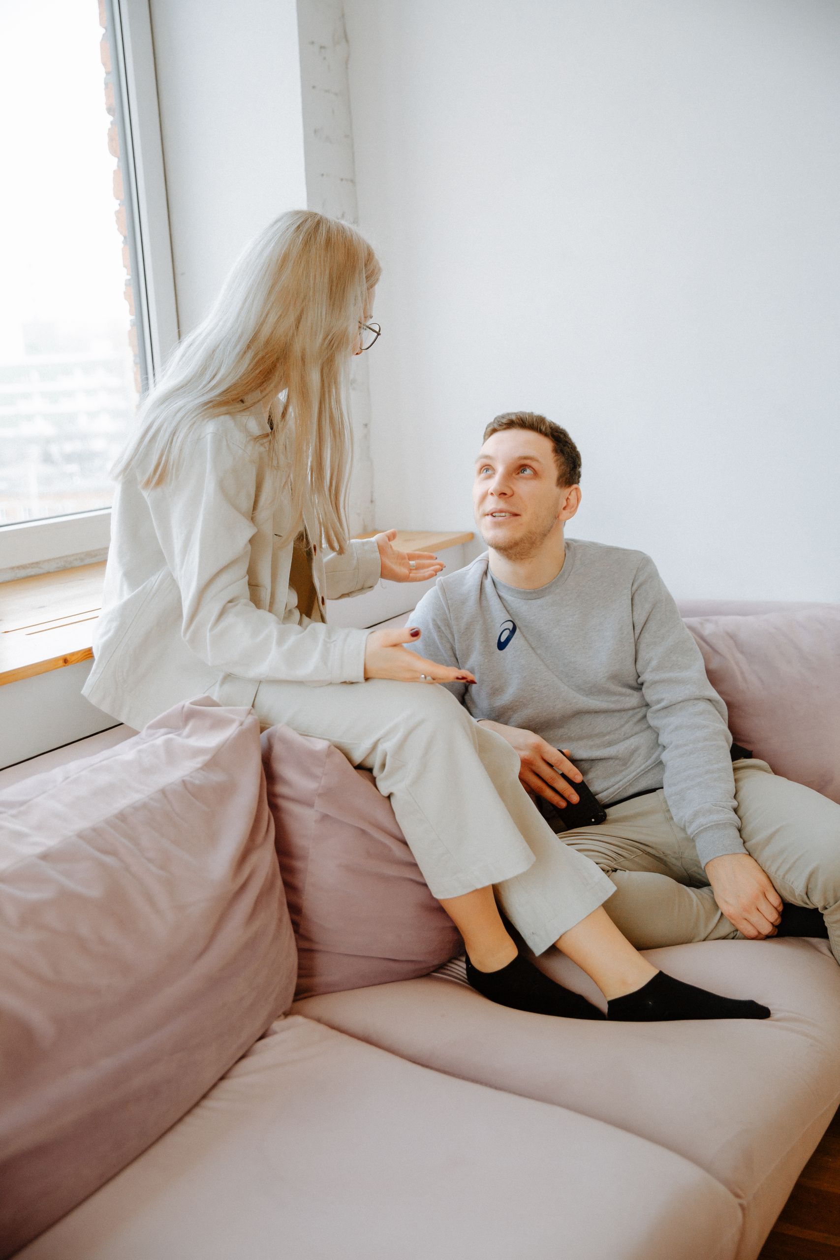 A couple having a conversation on a pink couch in a well-lit modern apartment.