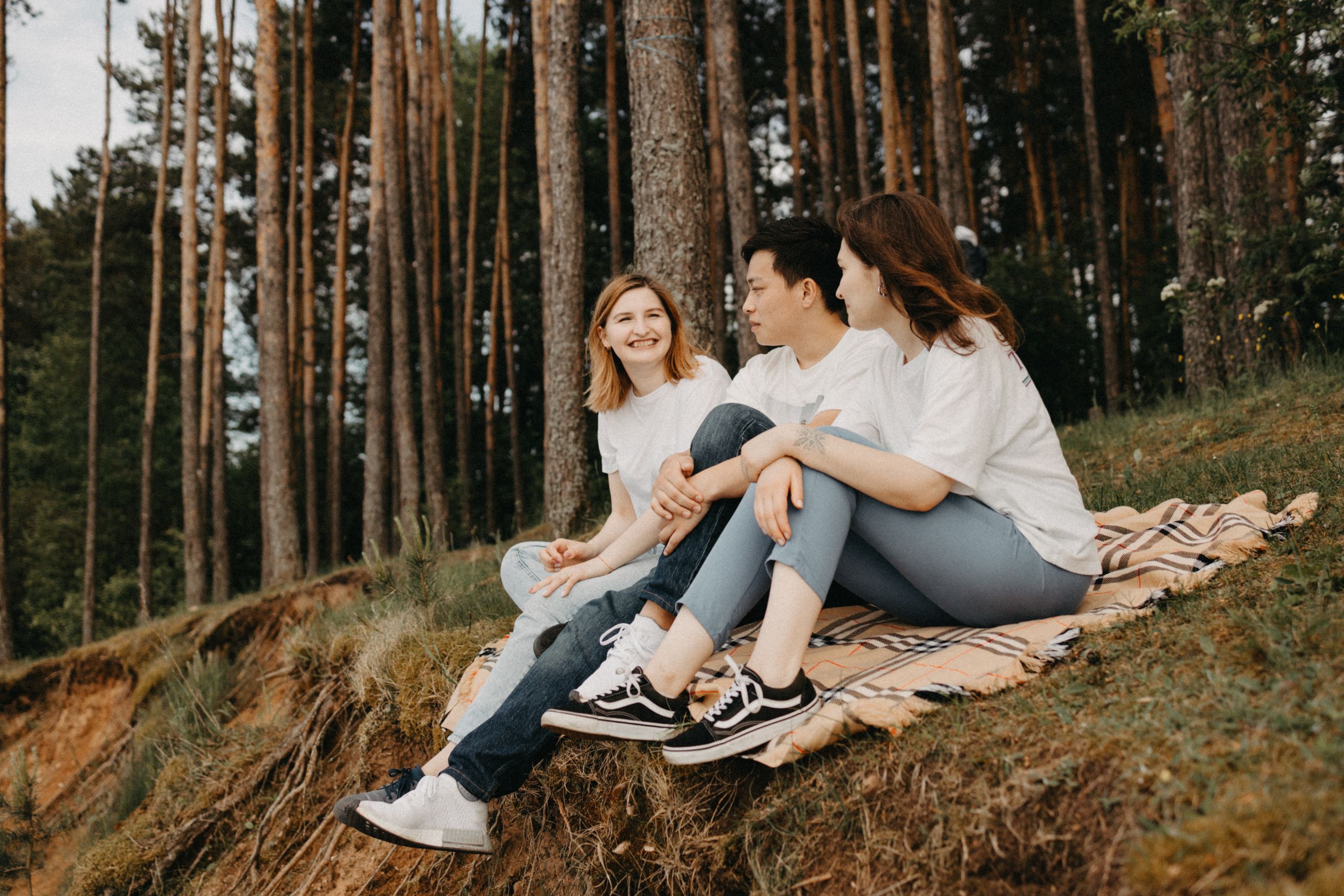 A group of friends enjoys a picnic on a blanket in a serene forest setting, sharing smiles and conversation.