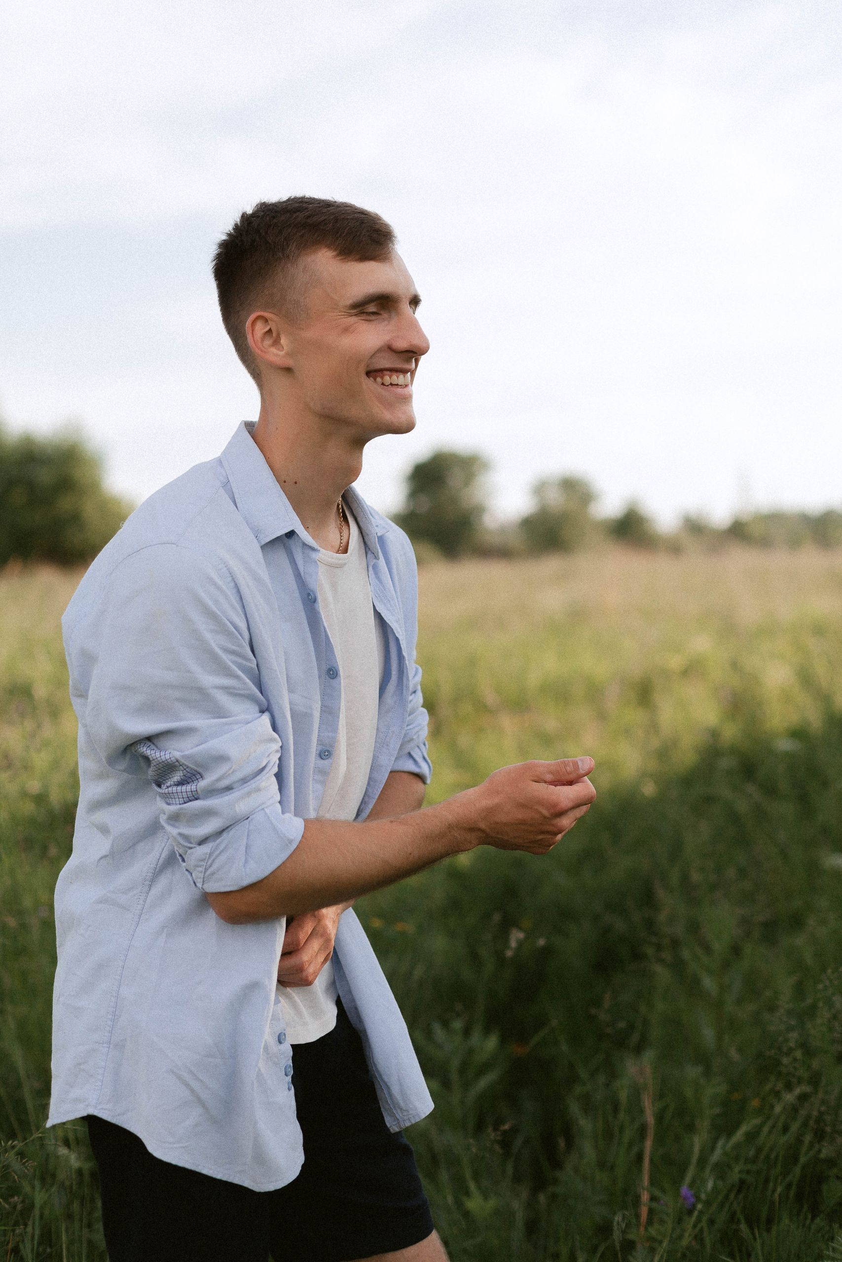 A handsome man in a field, smiling and enjoying the sunny outdoors.
