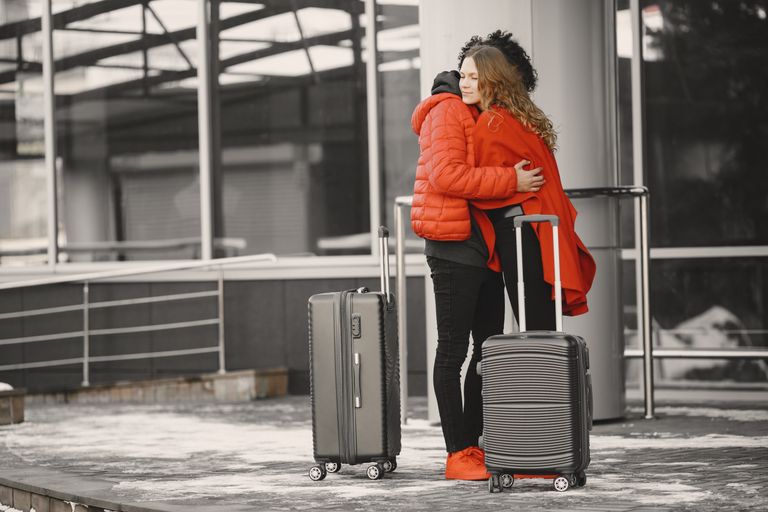 A heartfelt goodbye at the airport with two people hugging and luggage present.