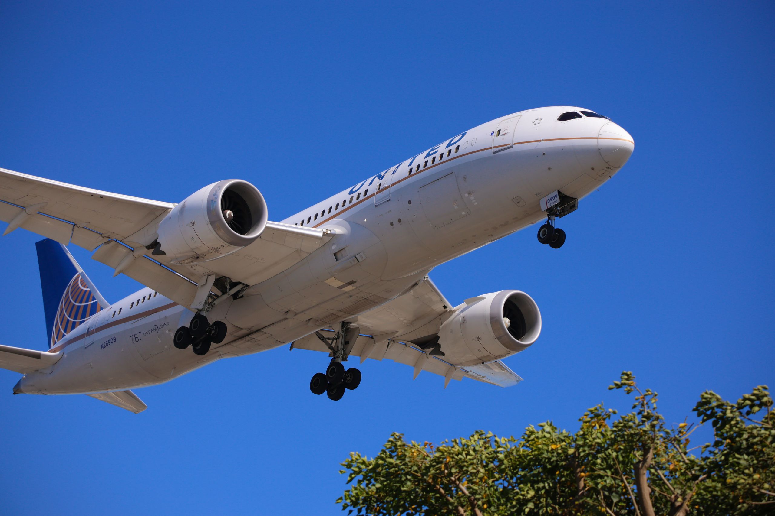 A large commercial airplane in flight with landing gear down, beneath a clear blue sky.