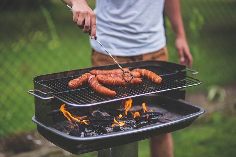 A man grills sausages over an open flame outdoors, perfect for summer cookouts.