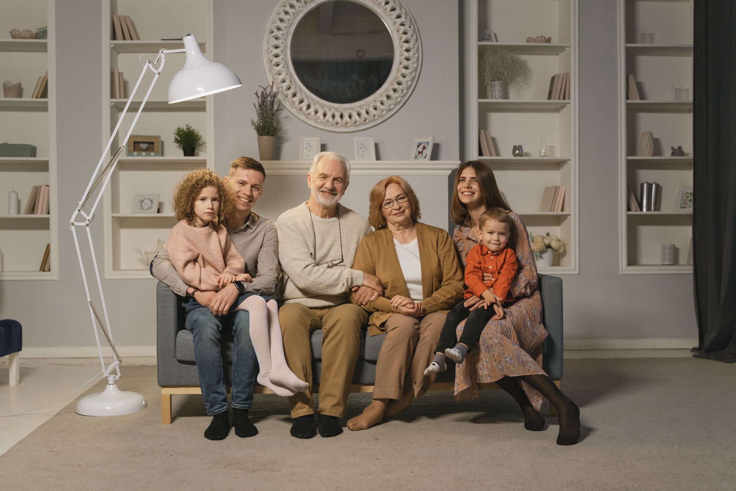 A multi-generational family sitting together on a sofa in a warm living room.