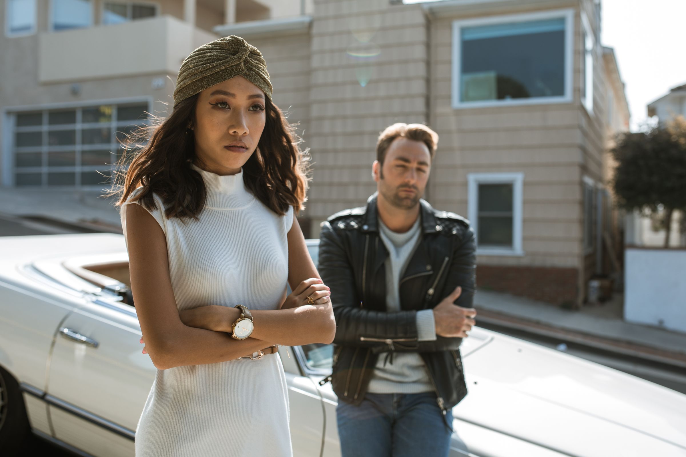 A couple standing apart on a sunny city street, visibly upset and not speaking to each other