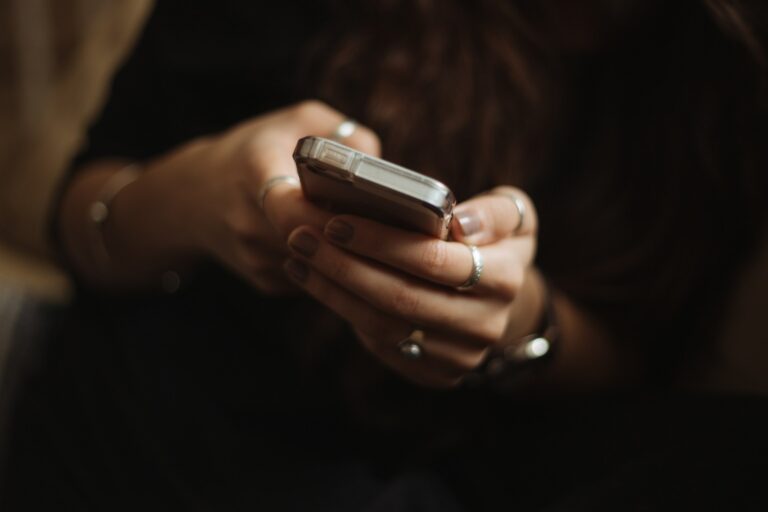 A woman holds a smartphone with soft natural light and a blurred background, representing singles using AI-powered dating apps