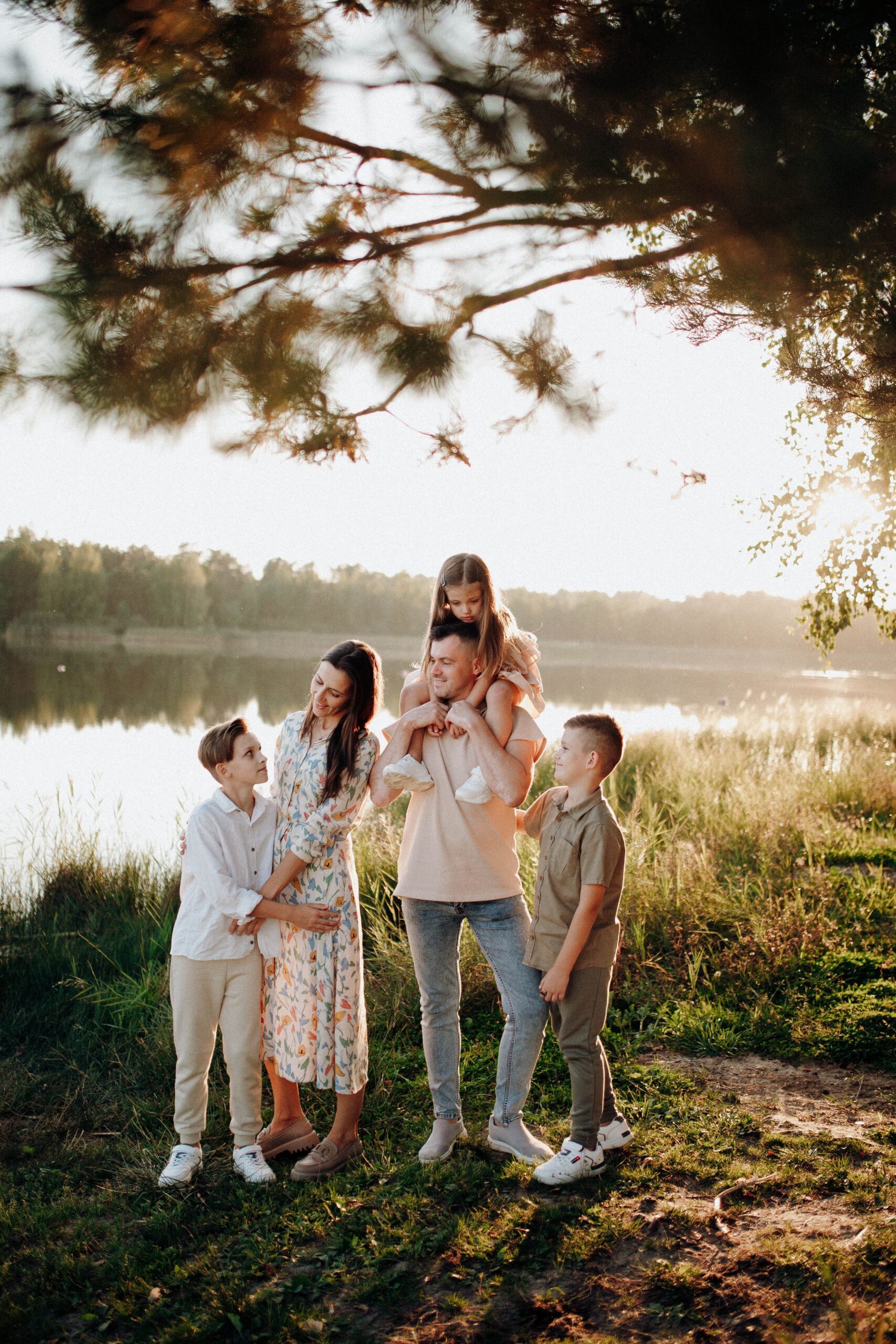 A family of five smiling together outdoors by a lake in natural sunlight, representing the kind of relaxed multi-parent gathering blended families work toward