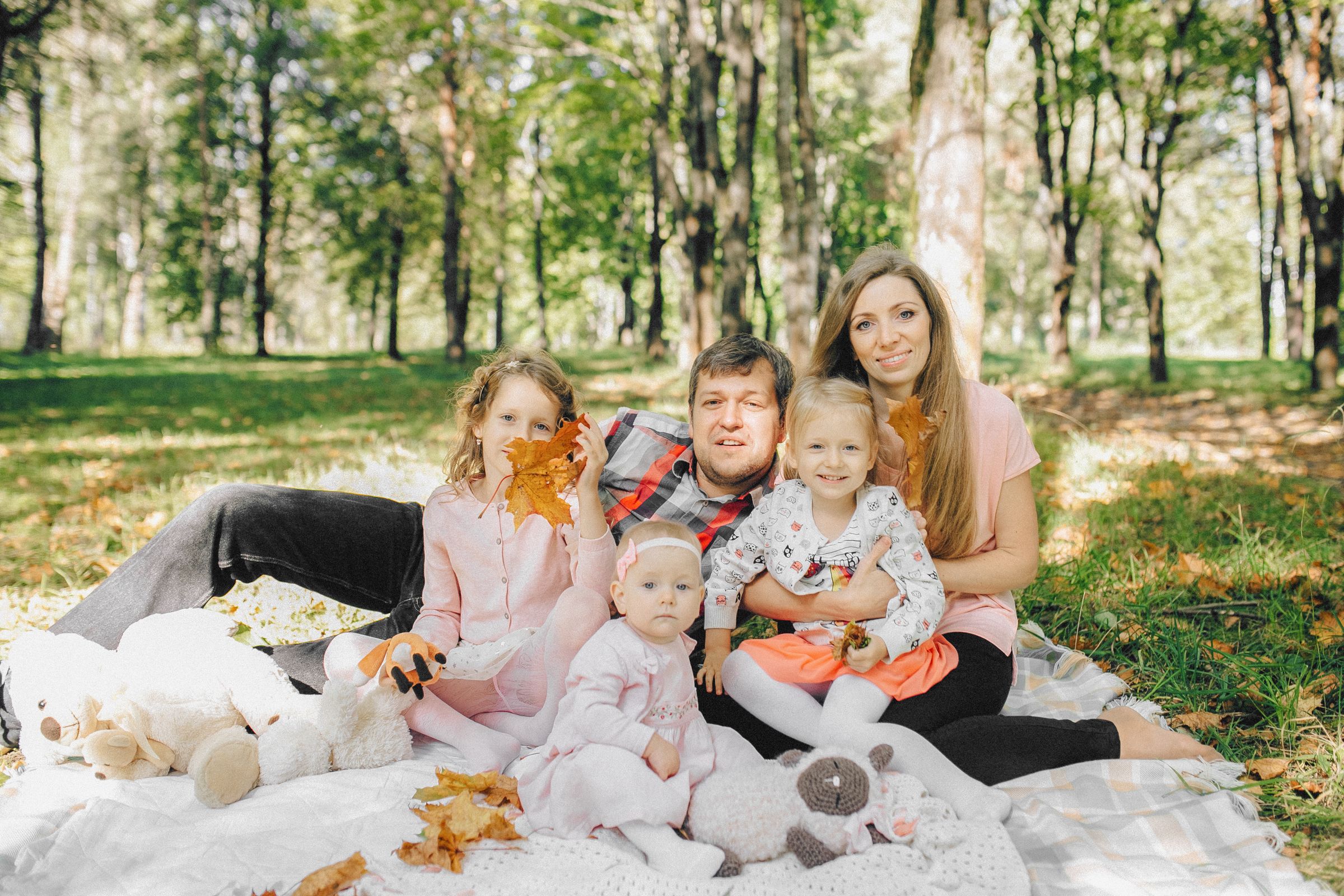 Two parents and their three children smiling together on a picnic blanket in a sunlit autumn forest, illustrating the everyday coordination behind a working blended family