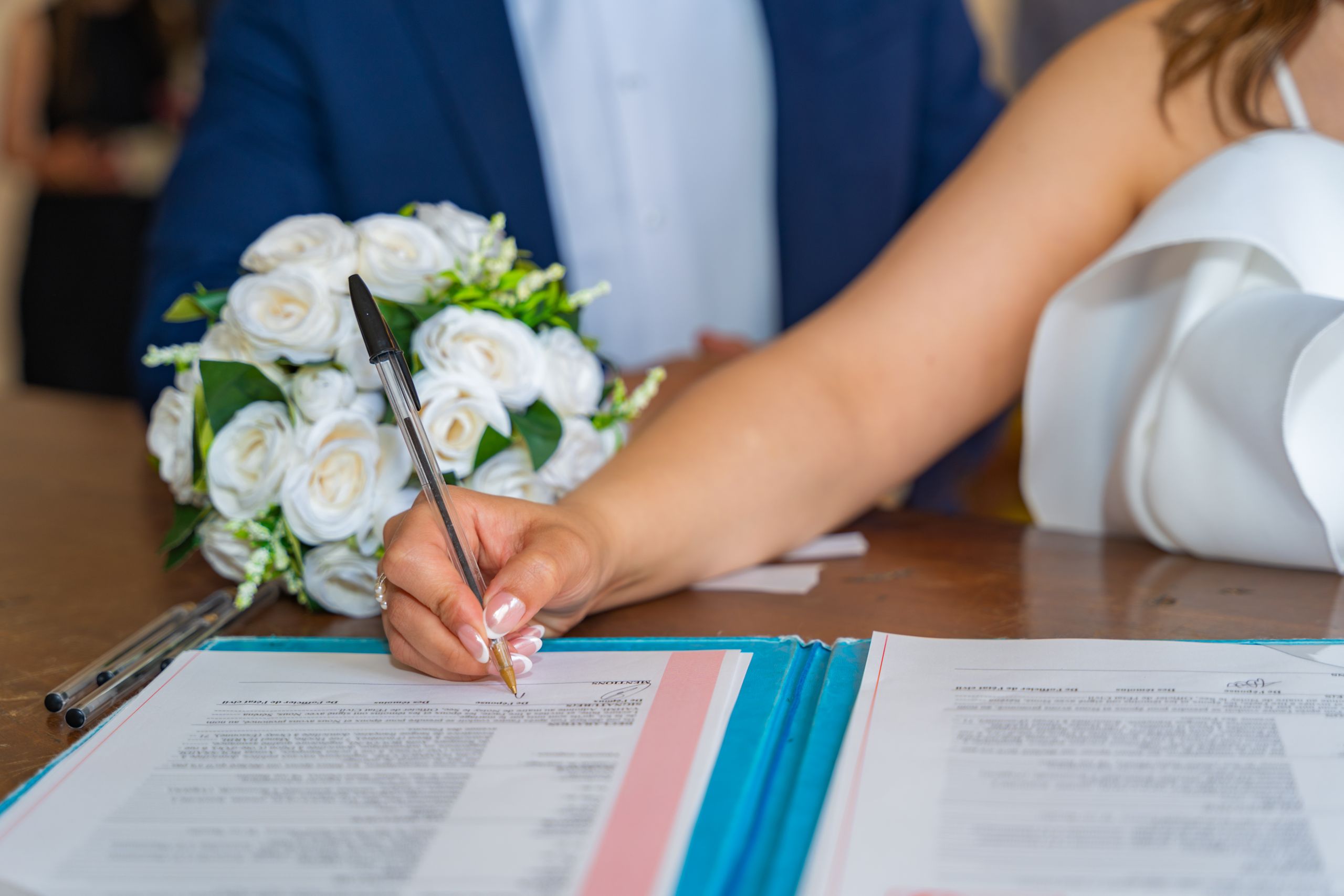 Bride signs marriage certificate during elegant indoor wedding ceremony, symbolizing commitment and togetherness.