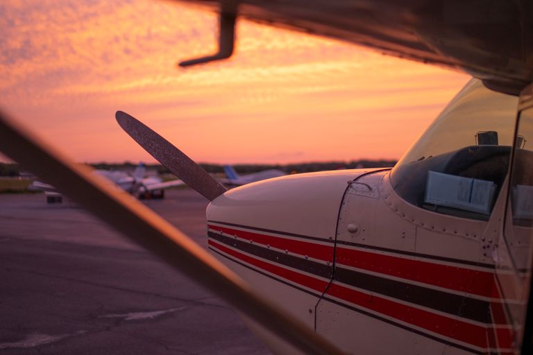 Close-up of a small propeller plane on the tarmac against a vibrant sunset sky, emphasizing aviation beauty.