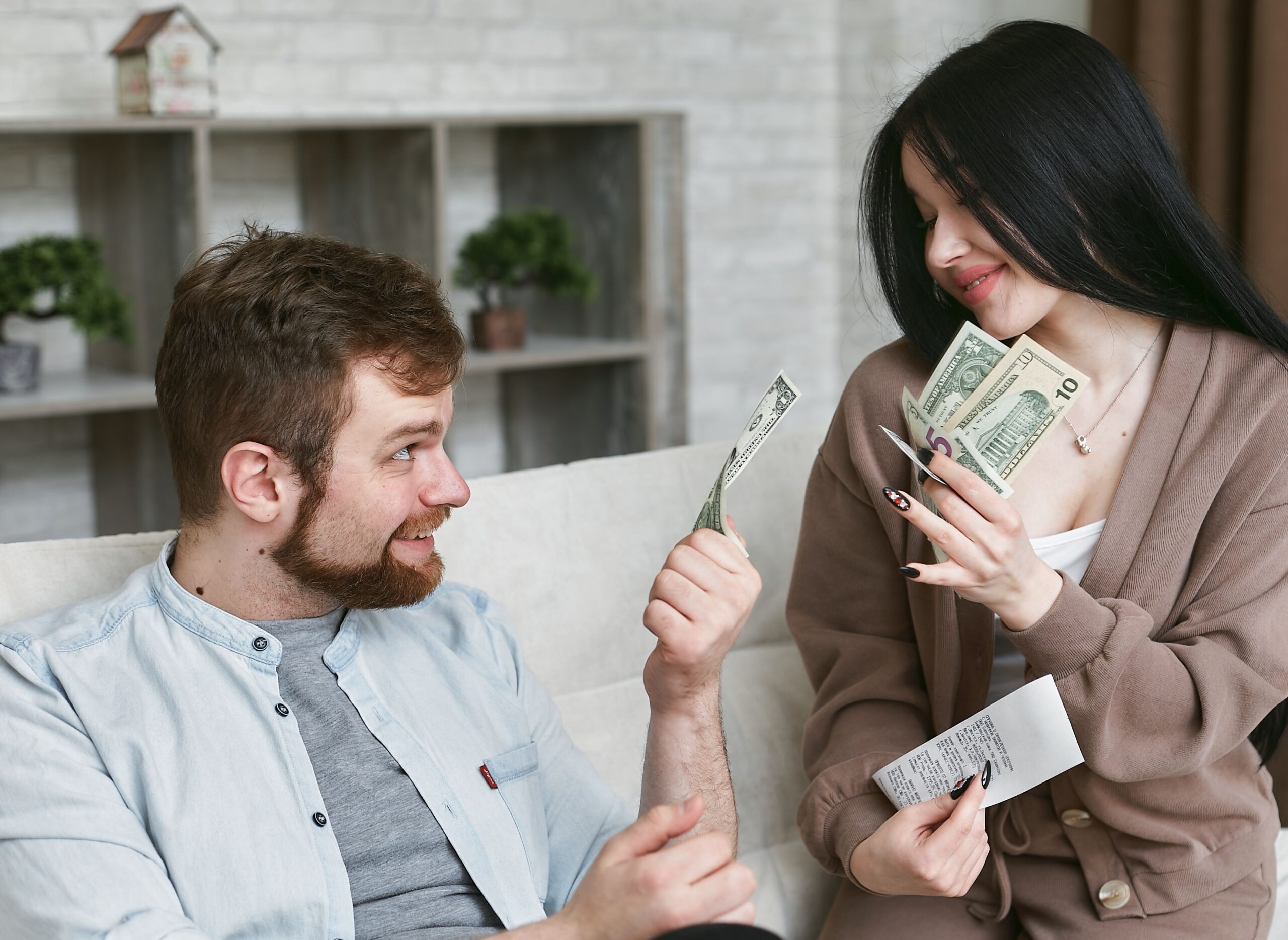 A couple sitting close together at home, smiling while going over cash and a receipt during a budgeting conversation