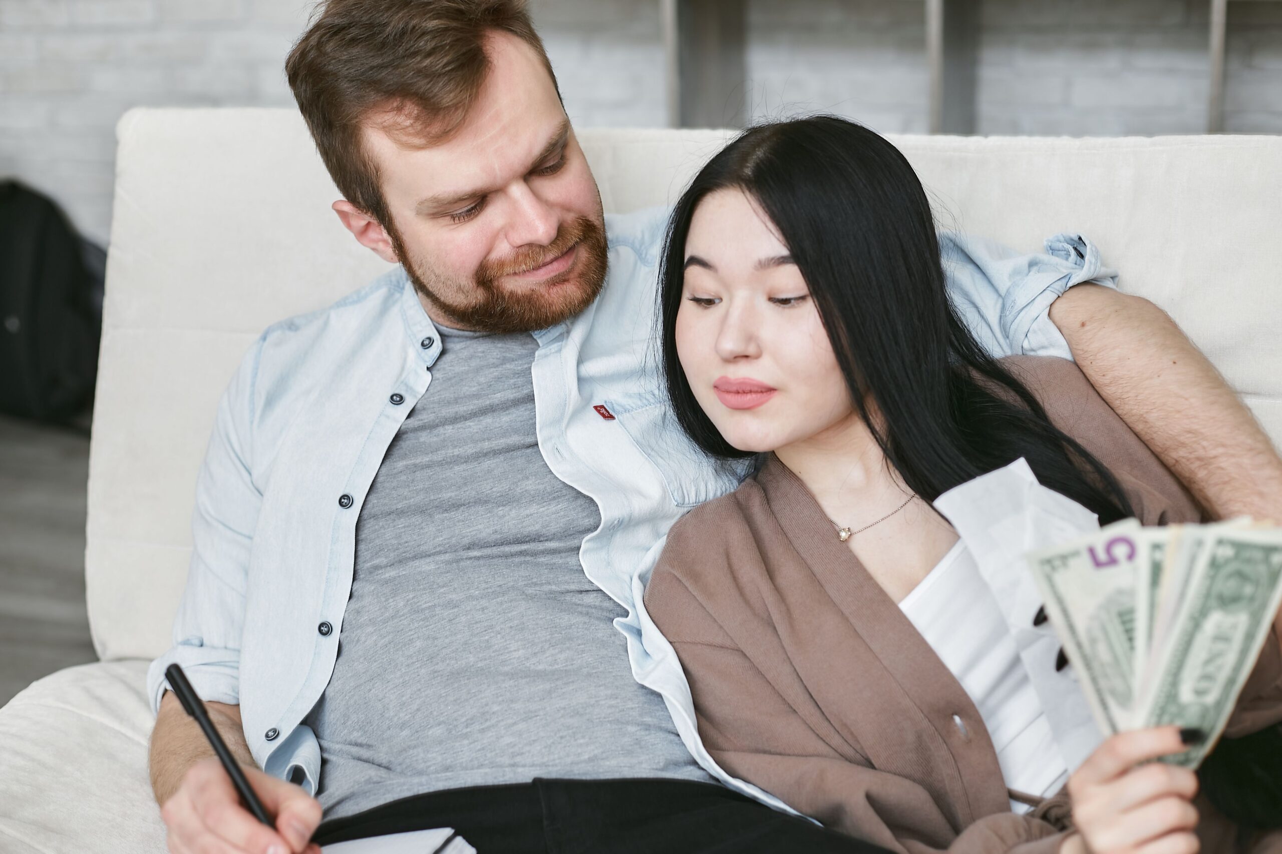 A couple sitting together on the sofa at home, warmly lit, looking over money and financial documents as they talk through their budget